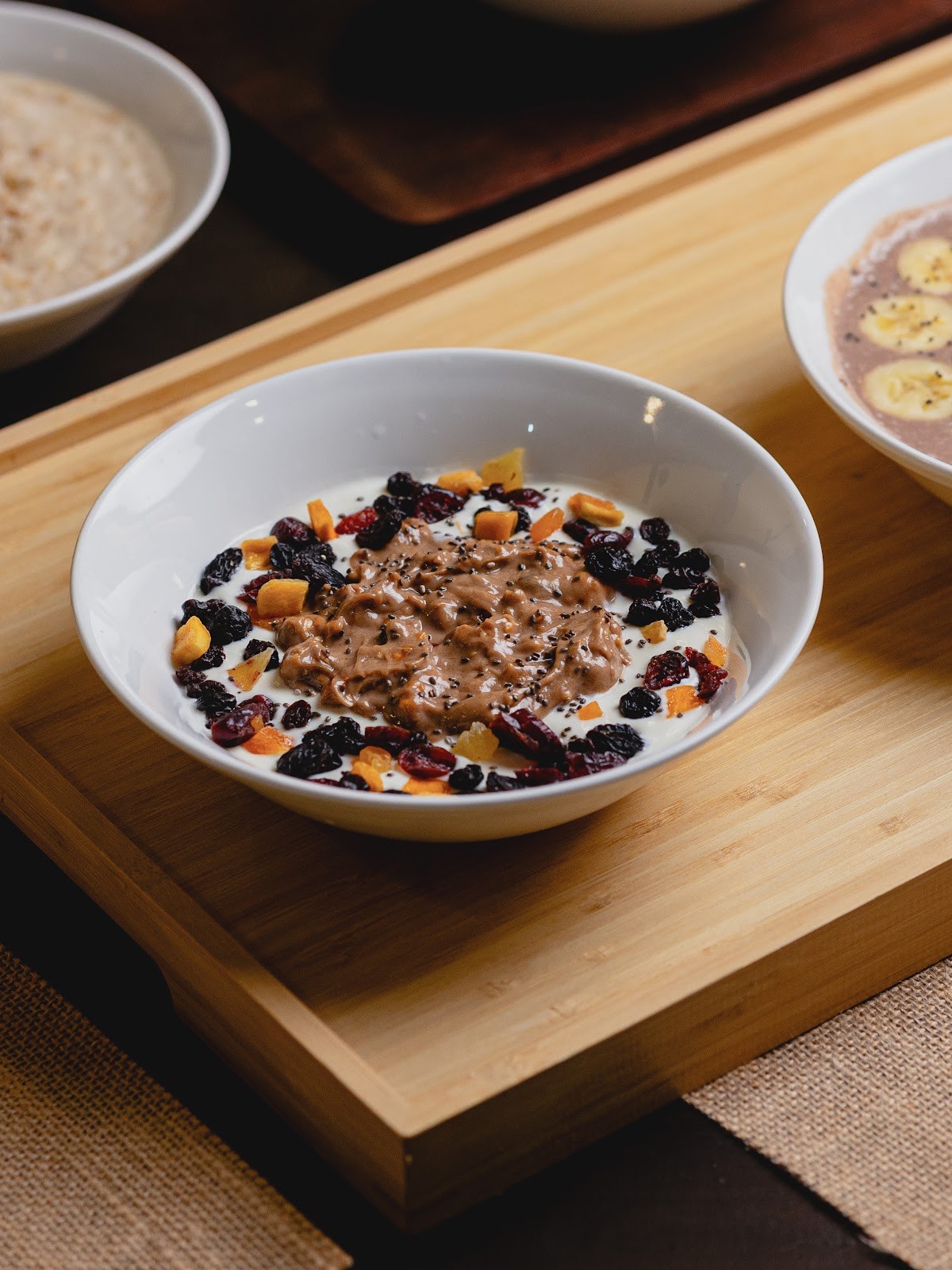 A yogurt bowl topped with peanut butter, dried cranberries and mango on a wooden serving board