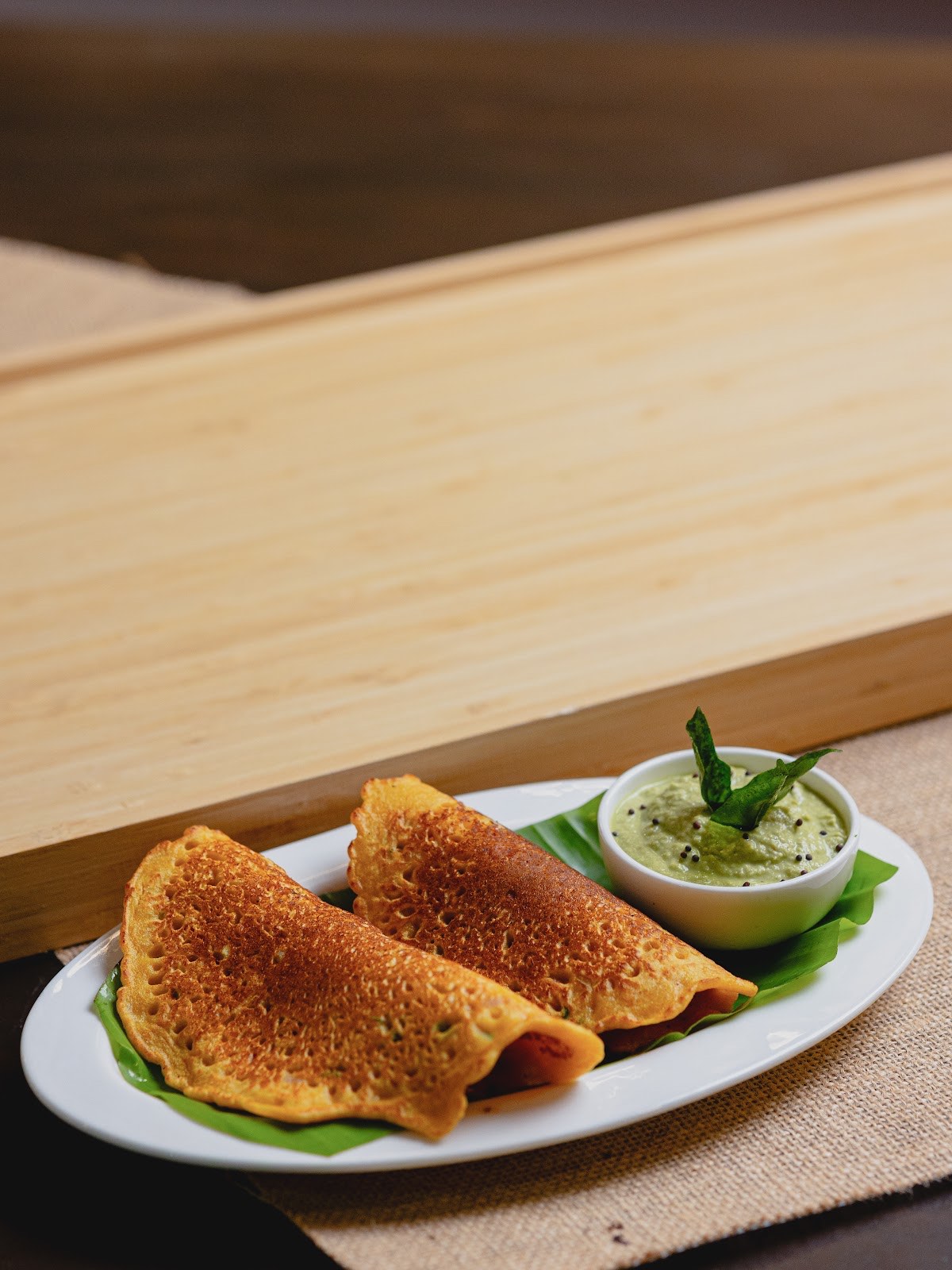 Two folded dosas on a banana leaf with a bowl of coriander chutney