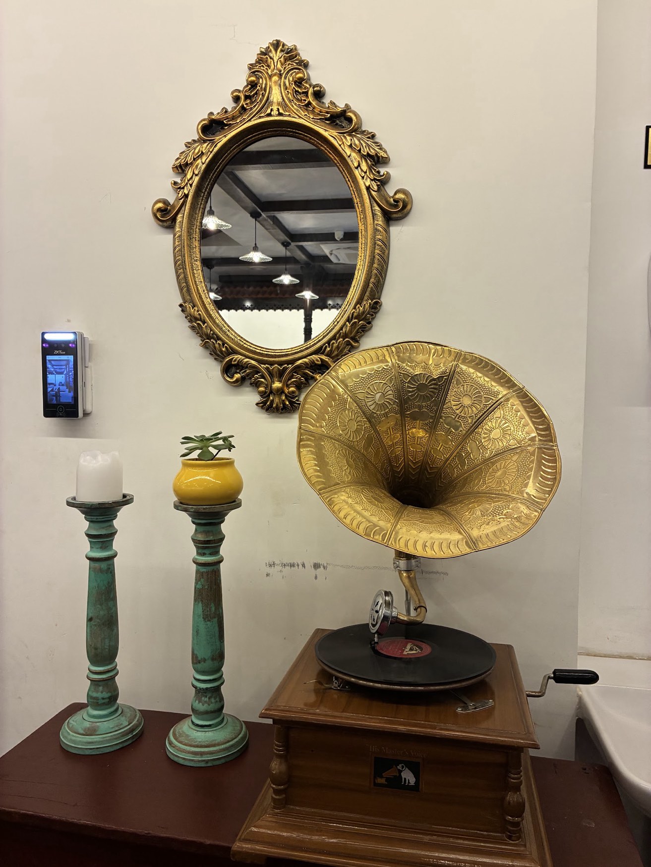 A brass gramophone with a gilt mirror above it and two green candlesticks alongside