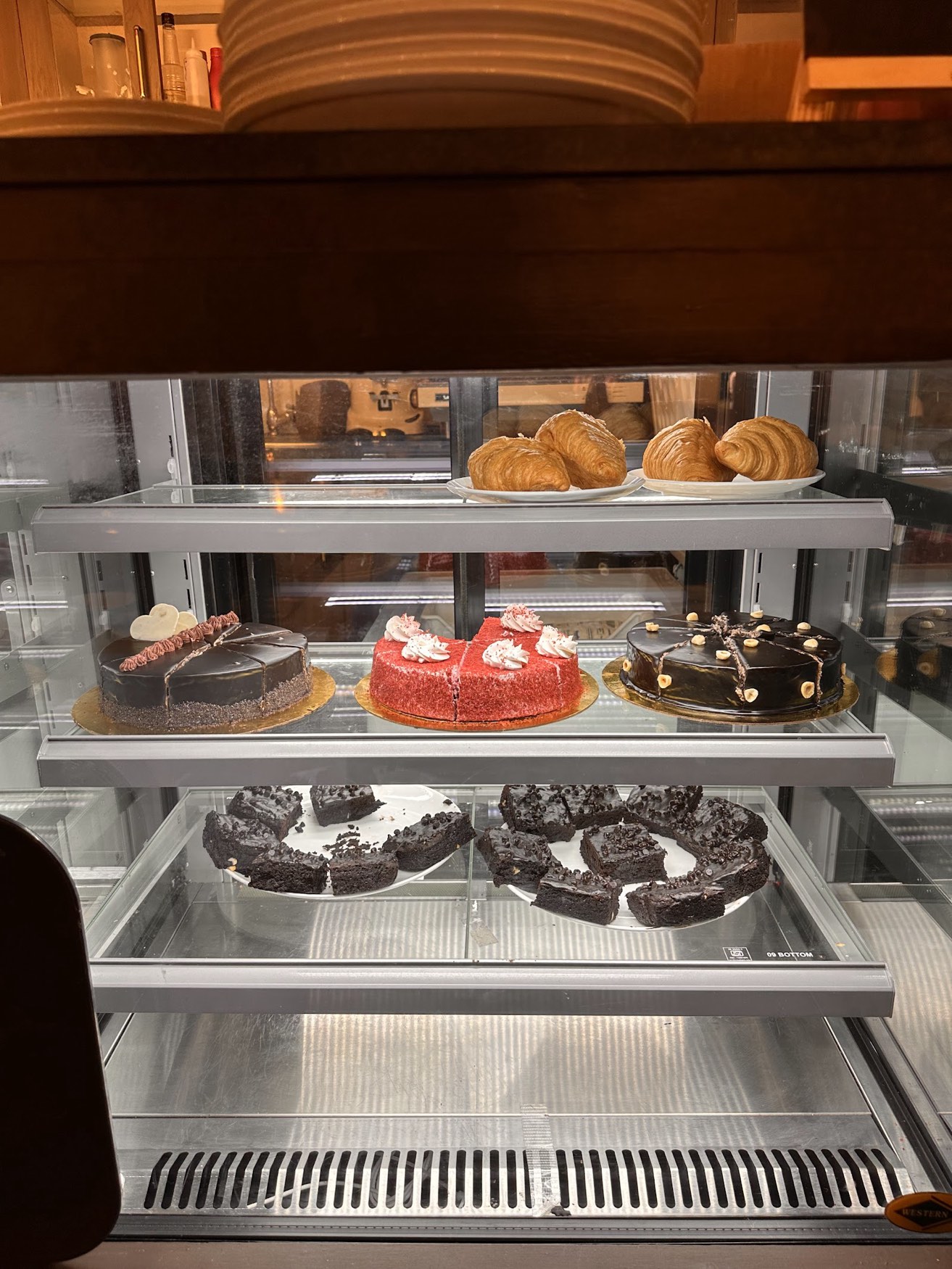 The dessert case by the counter — croissants, a chocolate tart, a pink cream cake and dark chocolate rounds